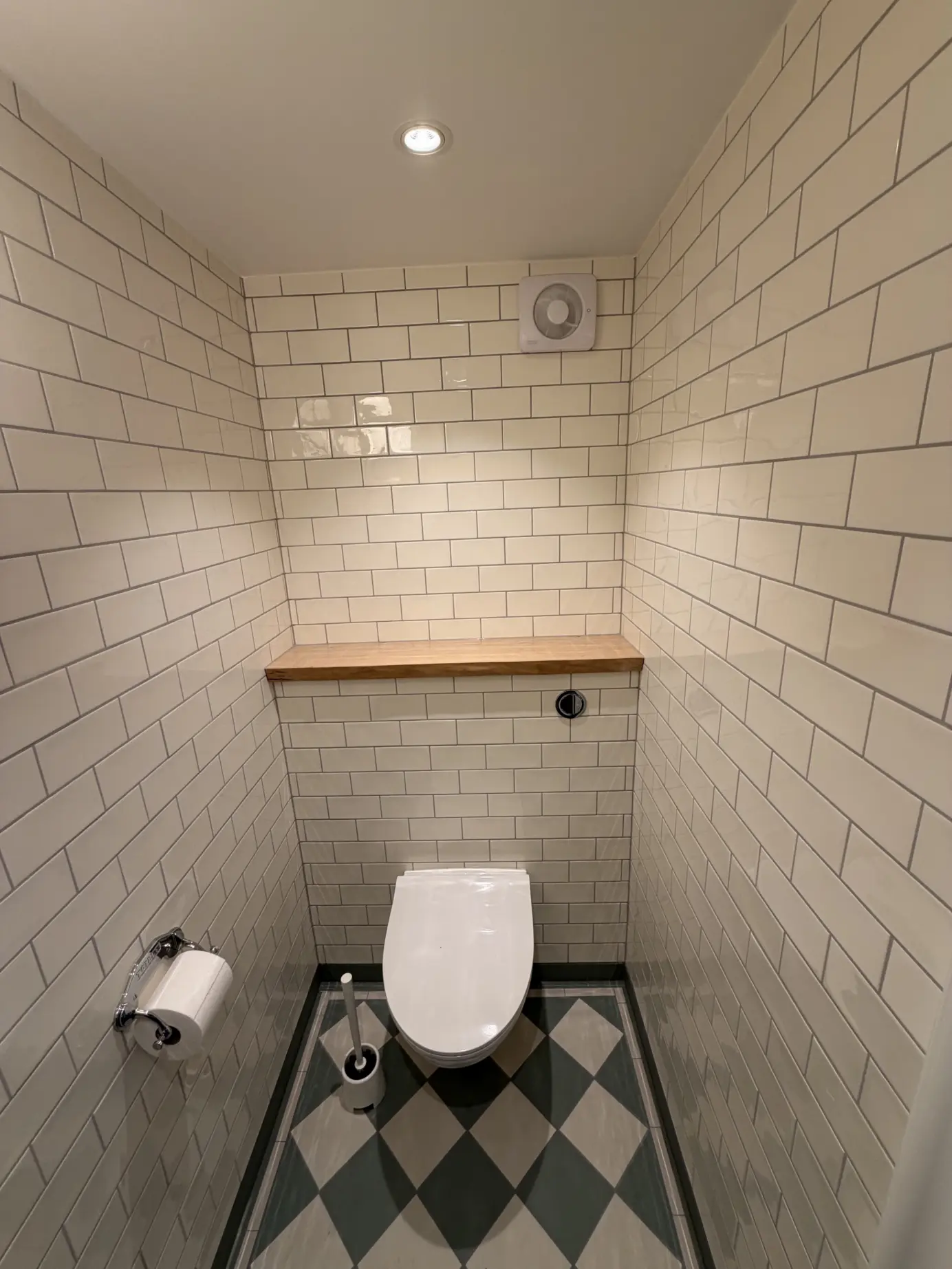 Toalett med vitt kakel och schackrutigt golv